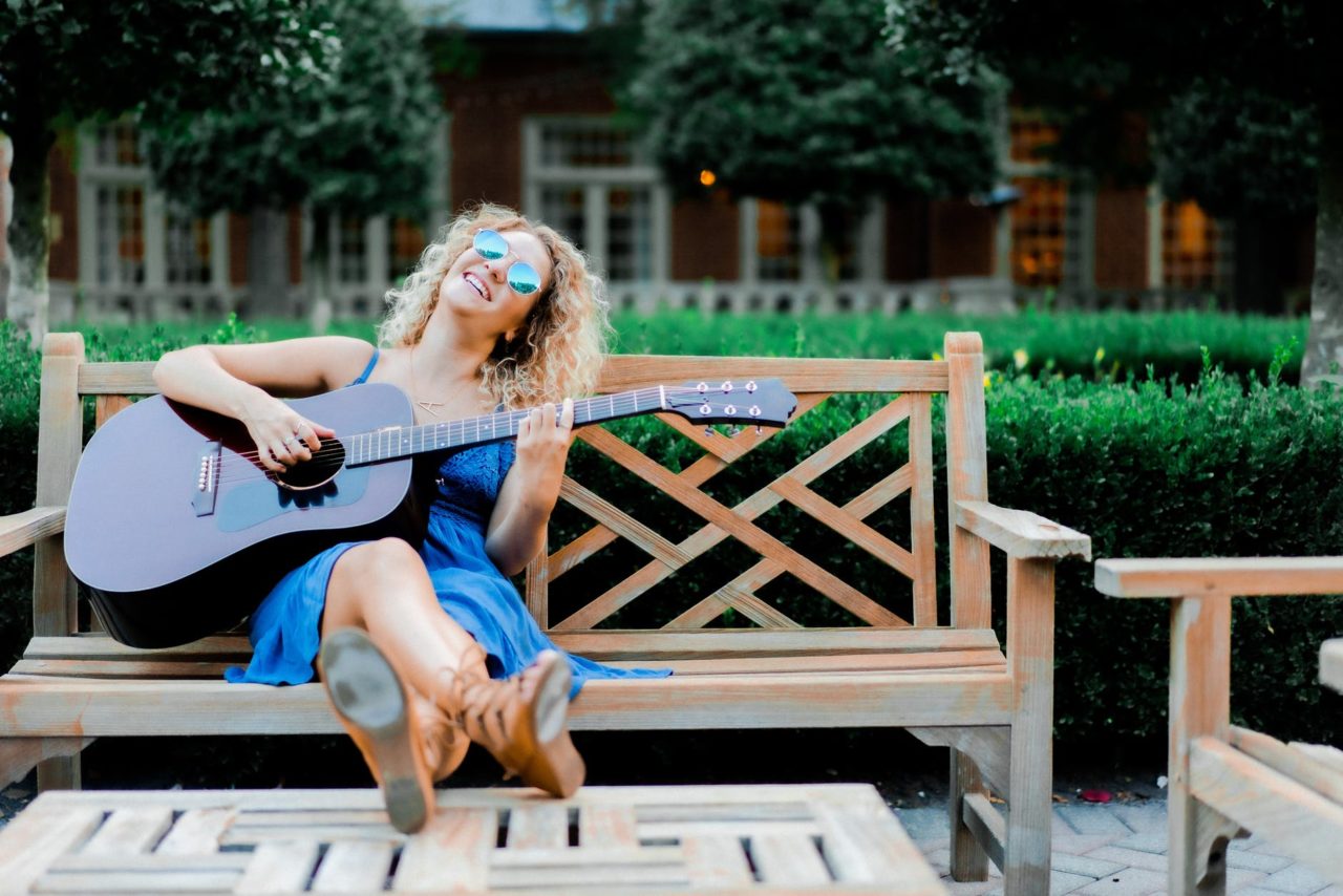 relaxed young lady playing guitar on bench in garden