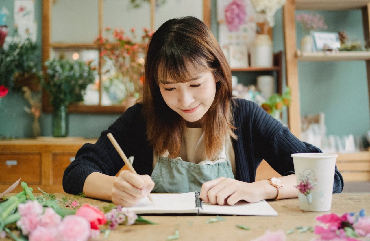 المحتوى امرأة آسيوية كتابة في دفتر في محل الأزهار